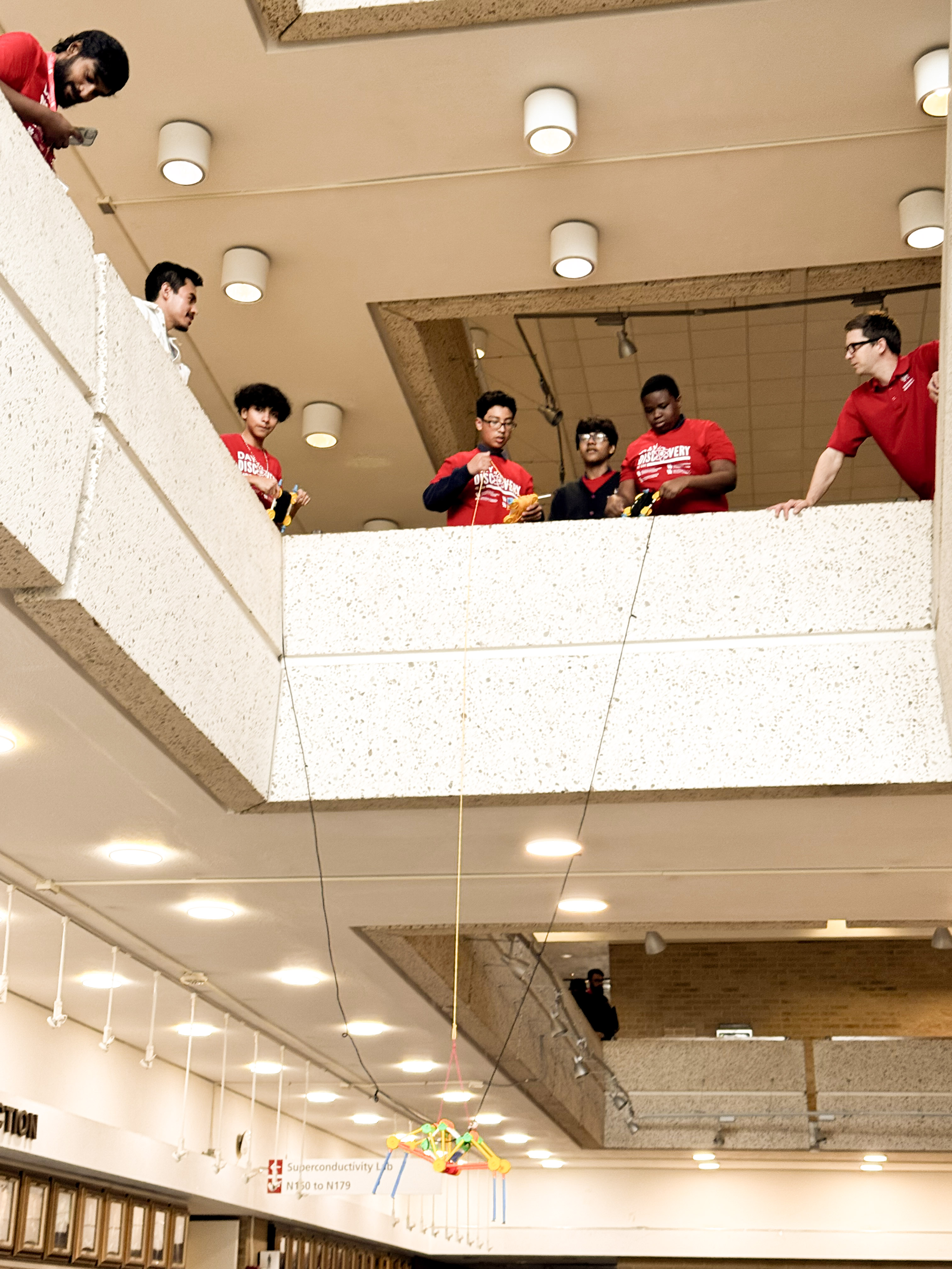 Students looking over a balcony while lowering a crane.