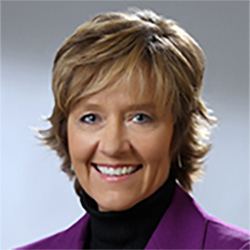 Protrait of woman with short blonde hair smiling wearing a purple jacket.