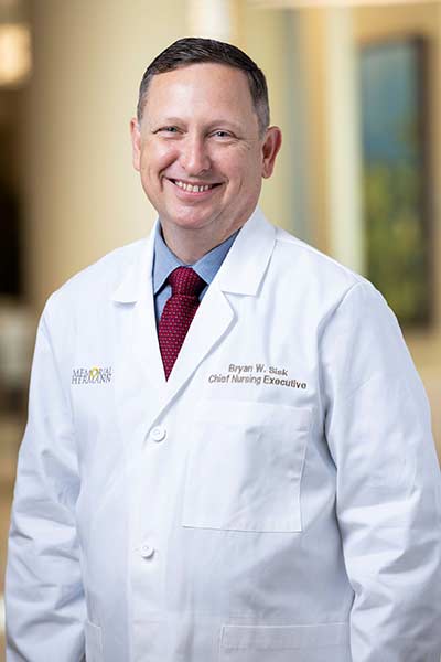 Portrait of a man smiling with short brown hair wearing a white lab coat with "Memorial Hermann" on the right front portion.