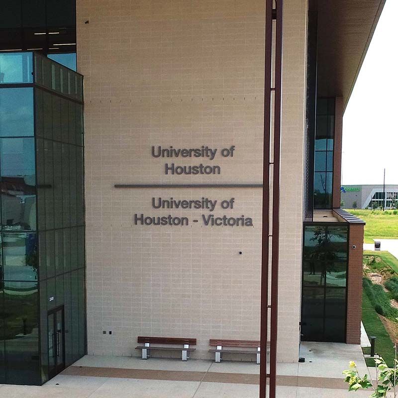 Photograph of a tall tan brick wall. Logos for the University of Houston and University of Houston - Victoria are visible.