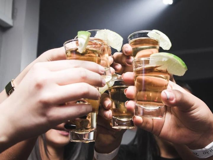 Group of people toasting with tequila shots garnished with lime slices.