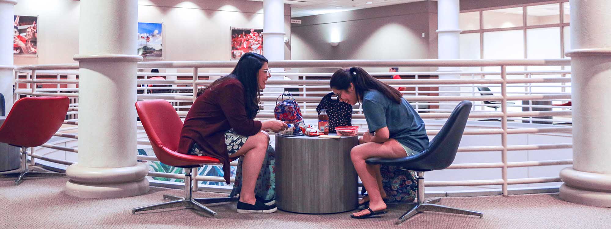 Two students facing each other, laughing, while eating lunch.