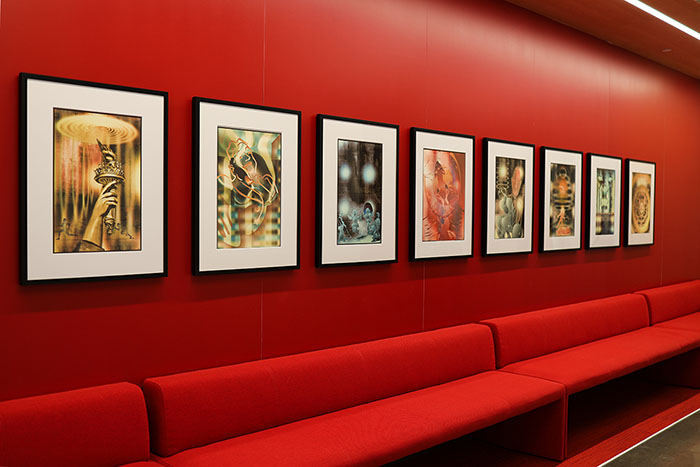 A collection of framed digital photographs on a red wall above red lounge seating