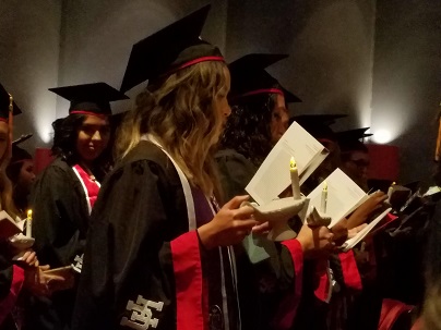 A group of students wearing graduation regalia and holding candles