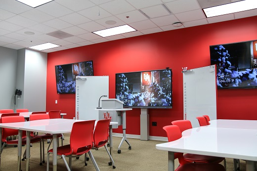 White tables in front of small podium. Three large television monitors are on the wall behind the podium