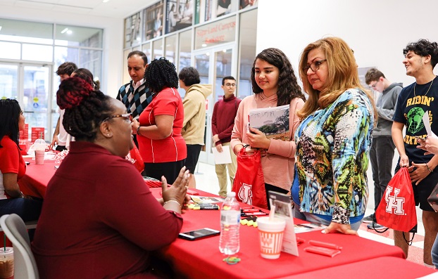 Women sitting at a red table talk to parents and their children as people wait in line