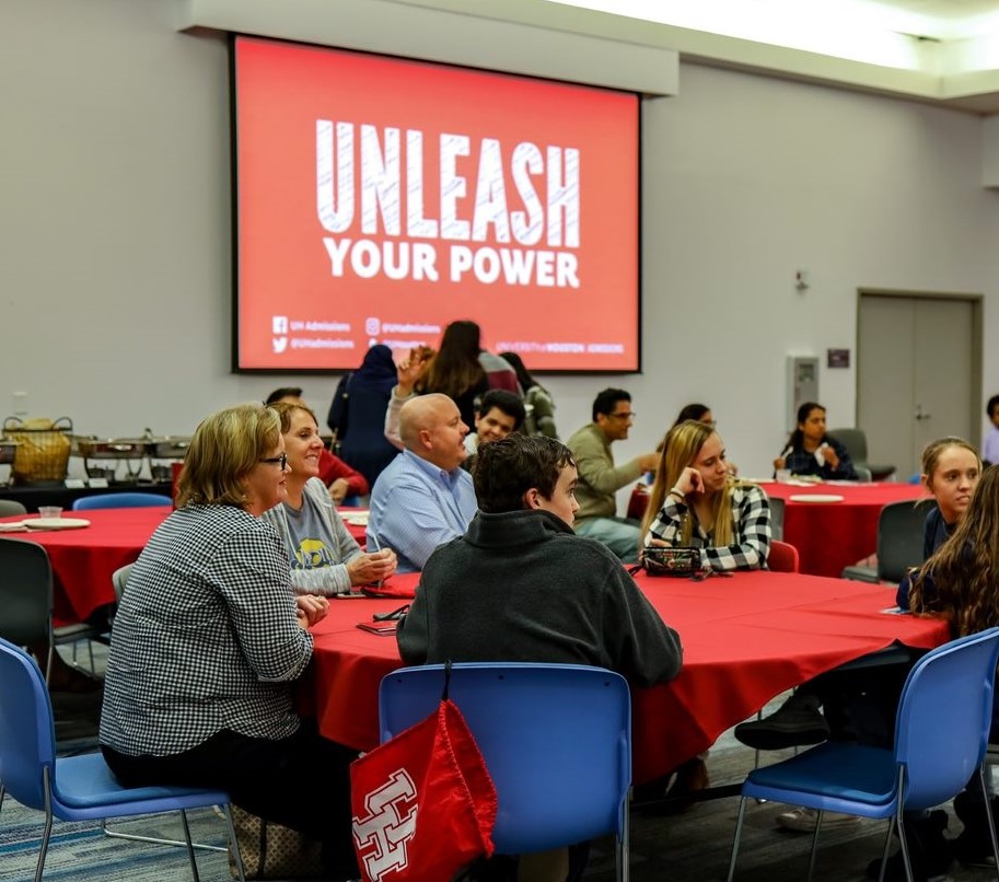 Parents and their children sitting at red banquet table with presentation on a projection screen in the background