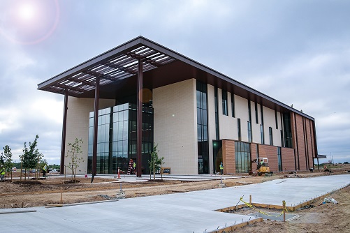 A three story building made of tan and brown bricks. The sidewalks and driveway are under construction.