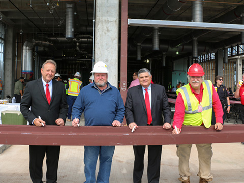 Four men standing behind metal beam holding markers