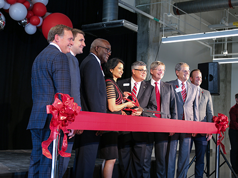 A group of people standing behind a red ribbon. Two people in the center are holding a pair of scissors.