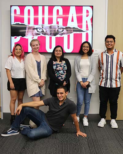 A group of students stand in front of a monitor that says "Cougar Proud".