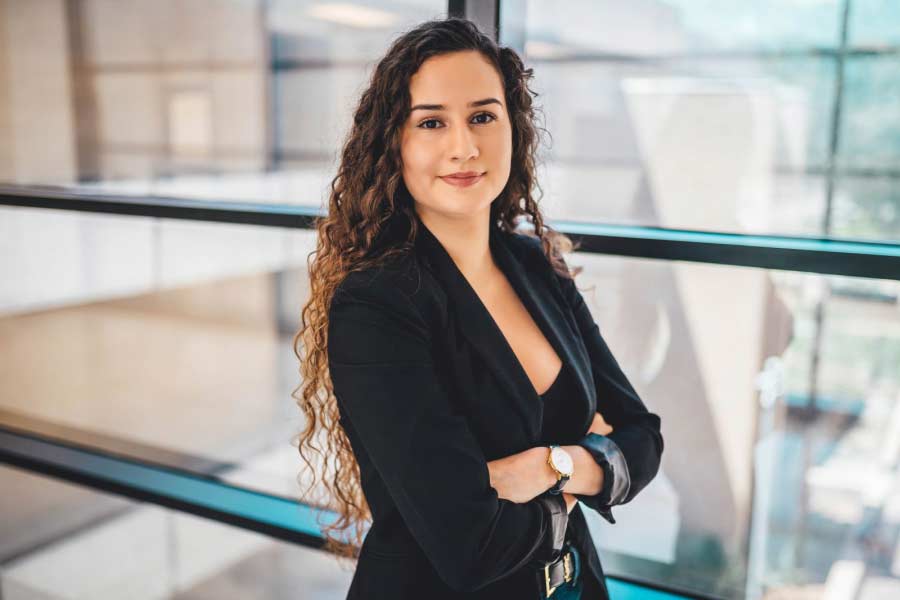 Portrait of a curly-haired white woman smiling with her arms crossed in a black business jacket.