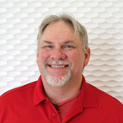 Portrait of a white man smiling with white hair and a circle beard wearing a red polo shirt